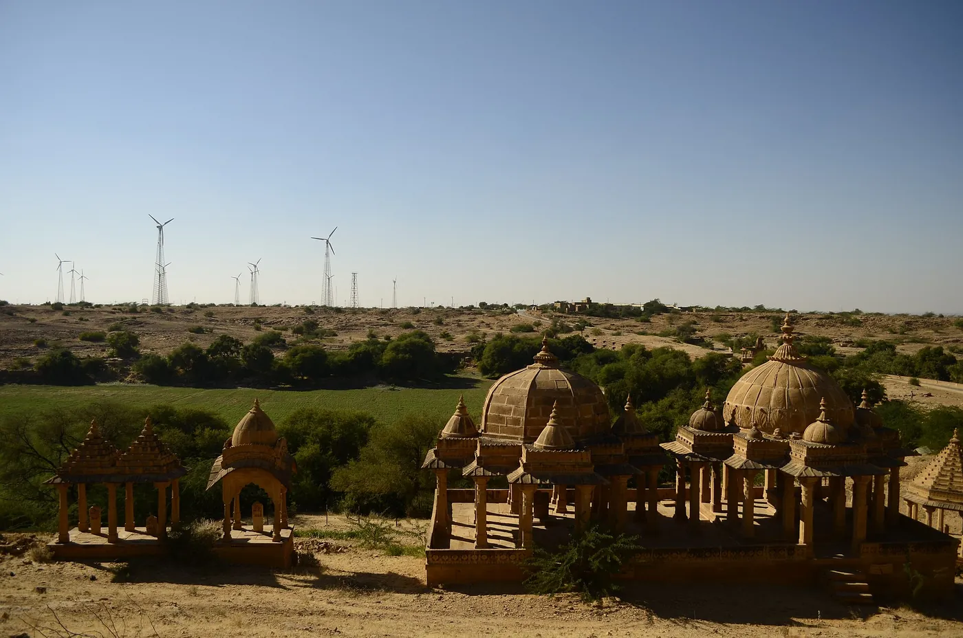 Wind turbines on the horizon behind sandstone cenotaphs near Jaisalmer